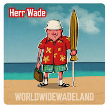 Herr Wade steht am Strand, mit Sonnenschirm und Sandalen